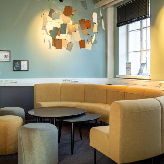 Business lab lokal för samarbete och lärande. På bilden syns en gul soffa, sittpuffar på golvet, runda bord med stolar. I taket hänger en handgjord armatur med anteckningslappar.