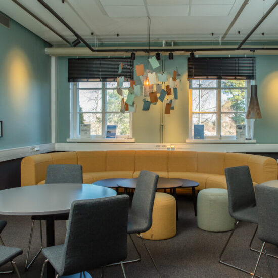 Business lab lokal för samarbete och lärande. På bilden syns en gul soffa, sittpuffar på golvet, runda bord med stolar. I taket hänger en handgjord armatur med anteckningslappar.