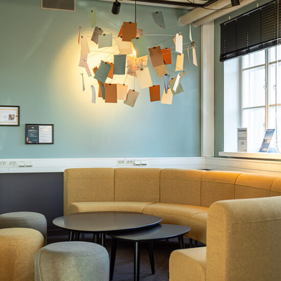 Business lab lokal för samarbete och lärande. På bilden syns en gul soffa, sittpuffar på golvet, runda bord med stolar. I taket hänger en handgjord armatur med anteckningslappar.